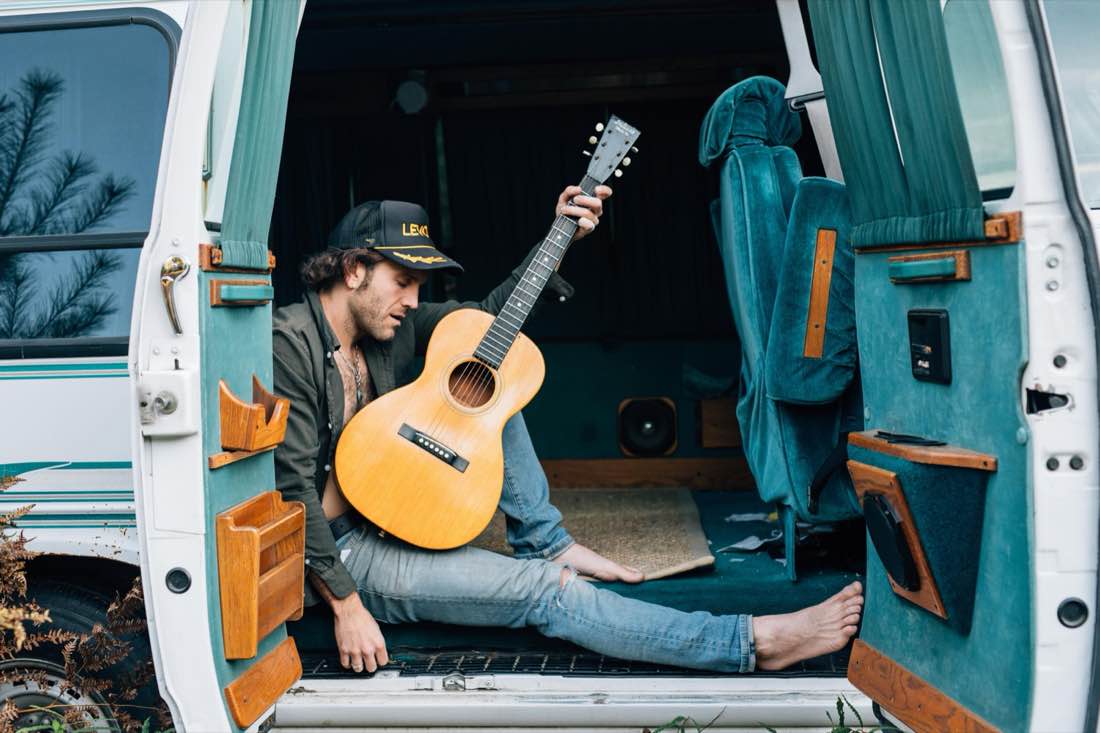 Musician playing guitar in the back of a tour van between shows